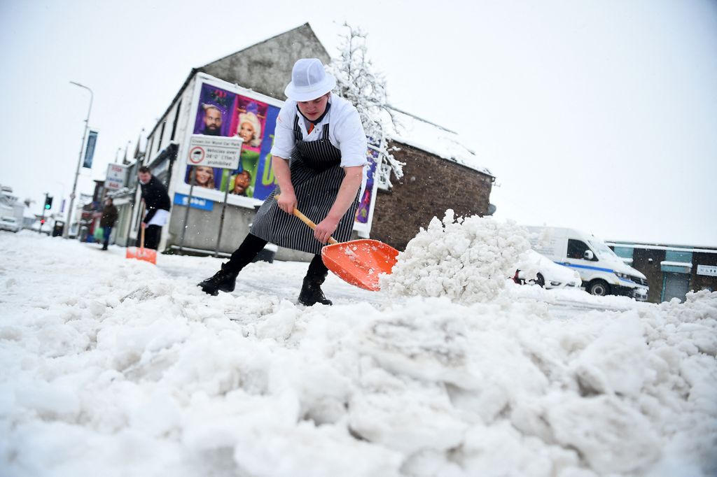 Butchers shovel the snow from the path outside their shop in Auchterarder, central Scotland, on February 18, 2022, as Storm Eunice brings high winds across the country. - Britain put the army on standby Friday and schools closed as forecasters issued two rare "red weather" warnings of "danger to life" from fearsome winds and flooding due to the approaching storm Eunice. (Photo by ANDY BUCHANAN / AFP)