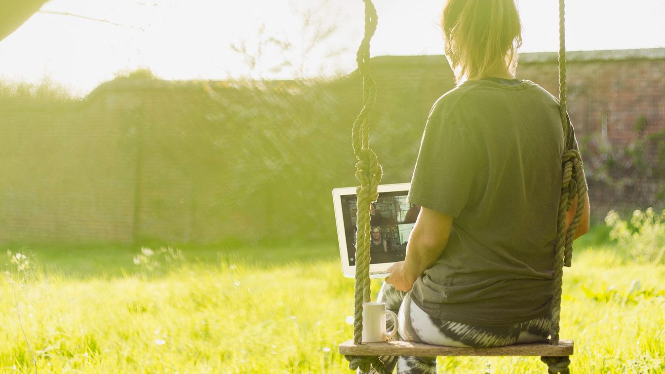 Woman with laptop video chatting on swing in sunny garden