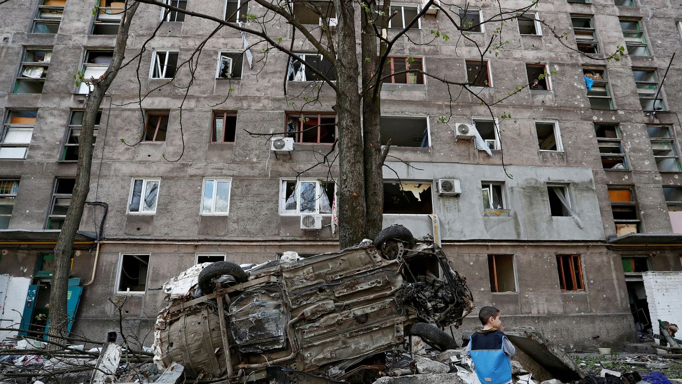 FILE PHOTO: A boy stands next to a wrecked vehicle in front of a damaged apartment building in Mariupol