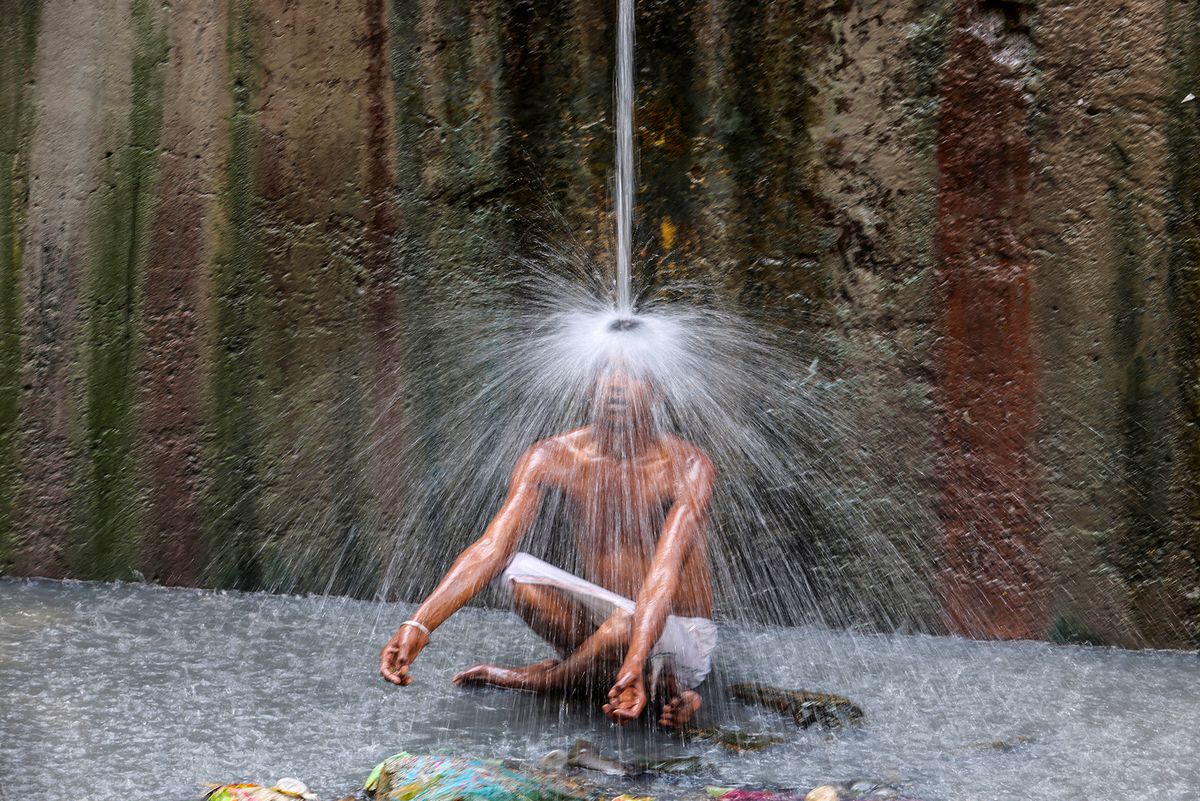 A man cools off under a pipe of flowing water on a hot summer day, in New Delhi