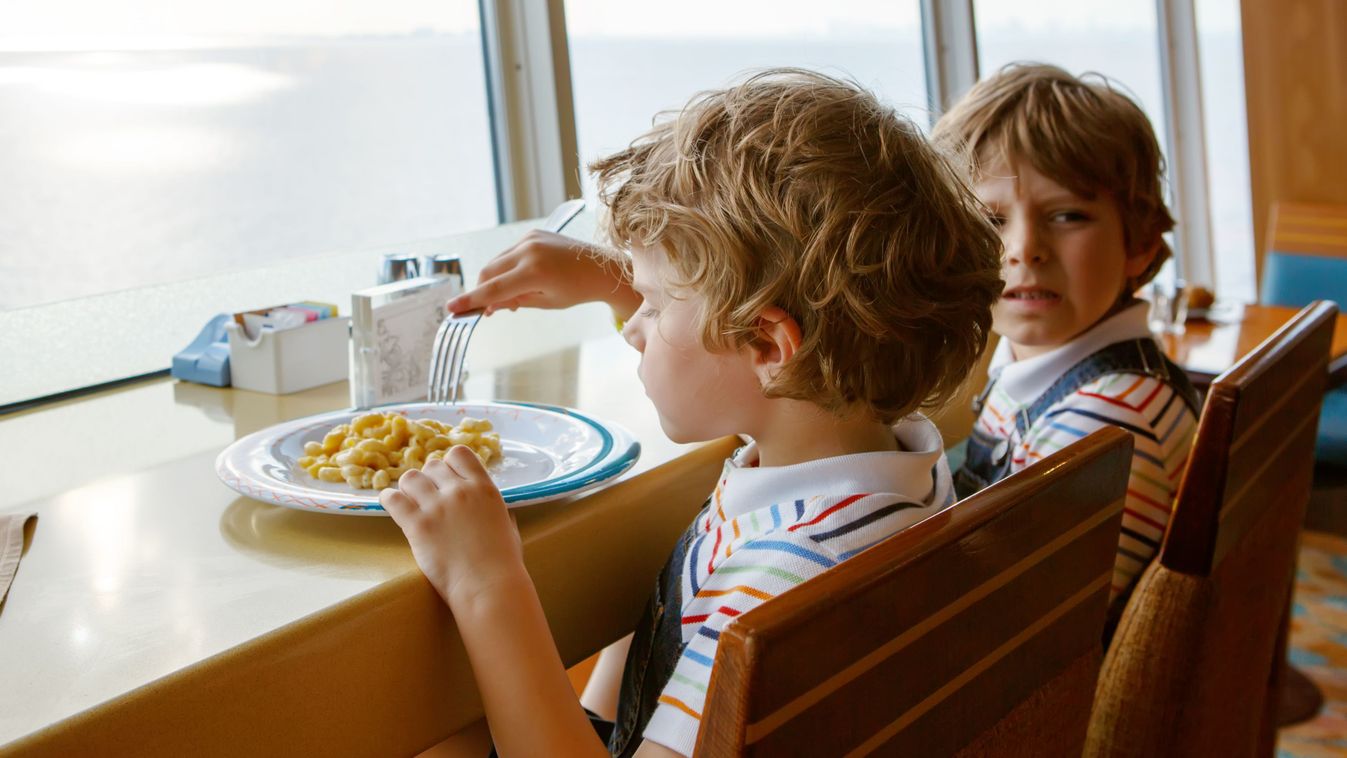 Two preschool kids boys eats pasta sitting in school canteen