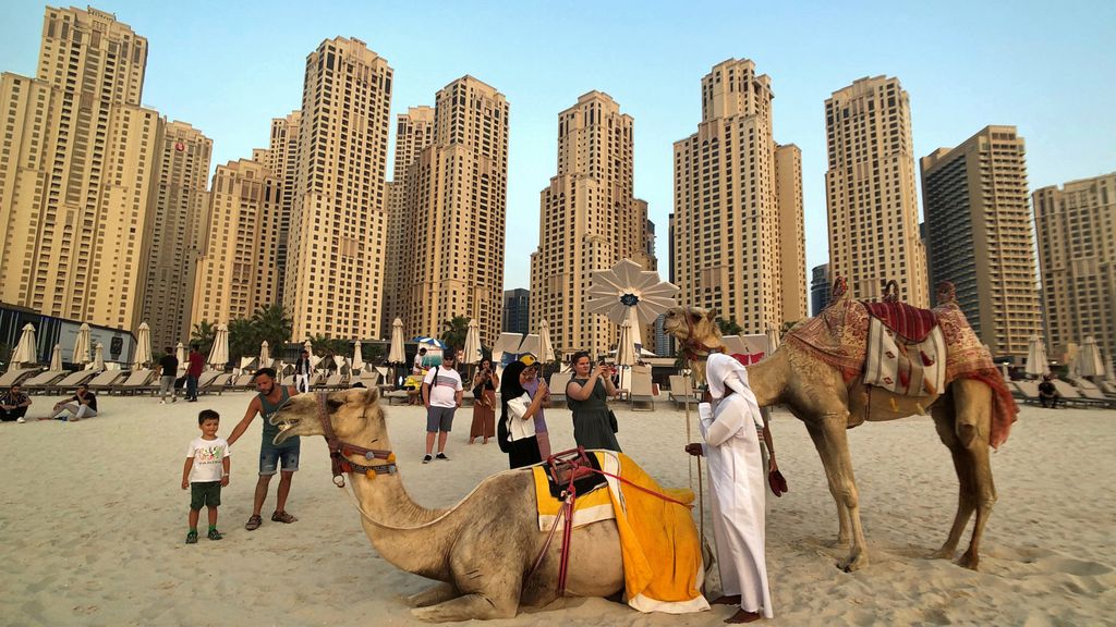 Tourists take photos with camels on the beach at Jumeirah Beach Residence in Dubai