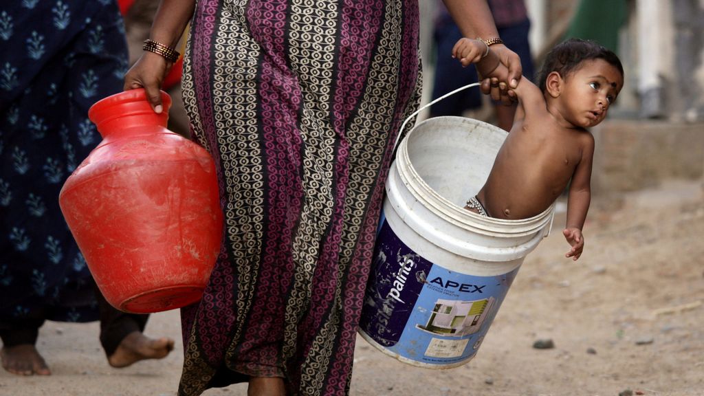 A woman carries her son in a bucket after collecting water from a municipal water tanker on the outskirts of Chennai