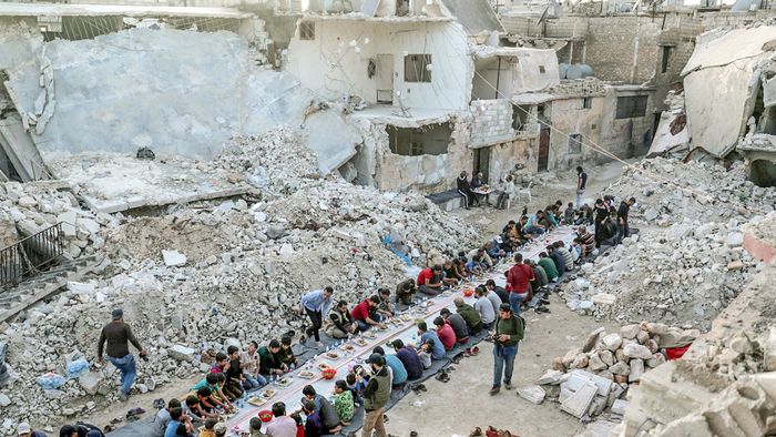 People eat their Iftar meal provided by a group of volunteers in a damaged neighbourhood, amid fear for the coronavirus disease (COVID-19) outbreak, in Atarib