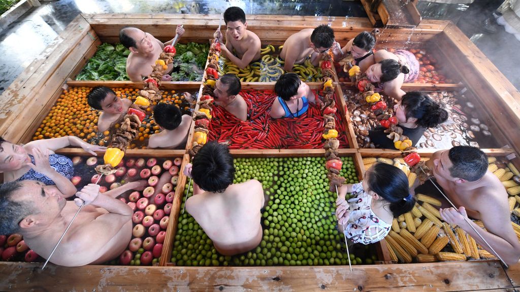 People enjoy a barbecue as they bath in a hotpot-shaped hot spring filled with fruits and vegetables, at hotel in Hangzhou