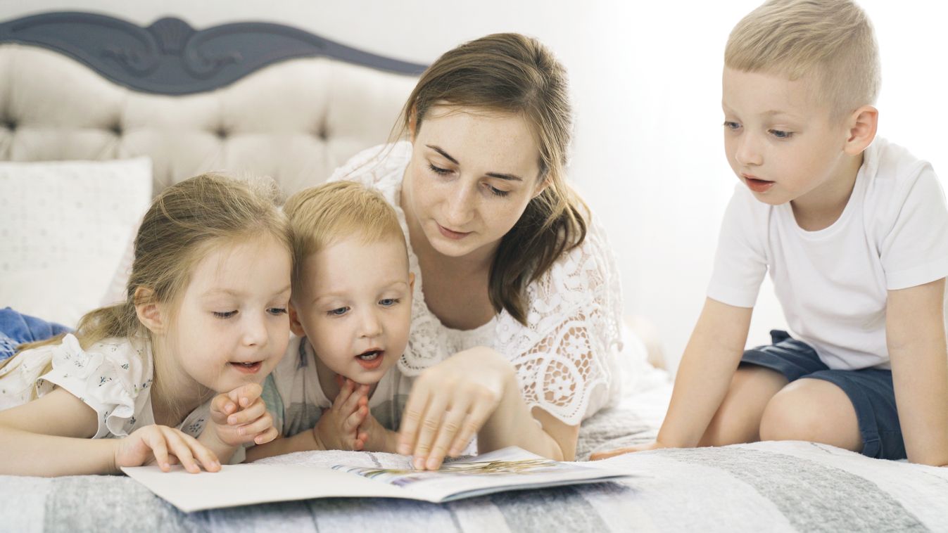 Children lie on the bed in the bedroom, mother reads a book to them.
mese