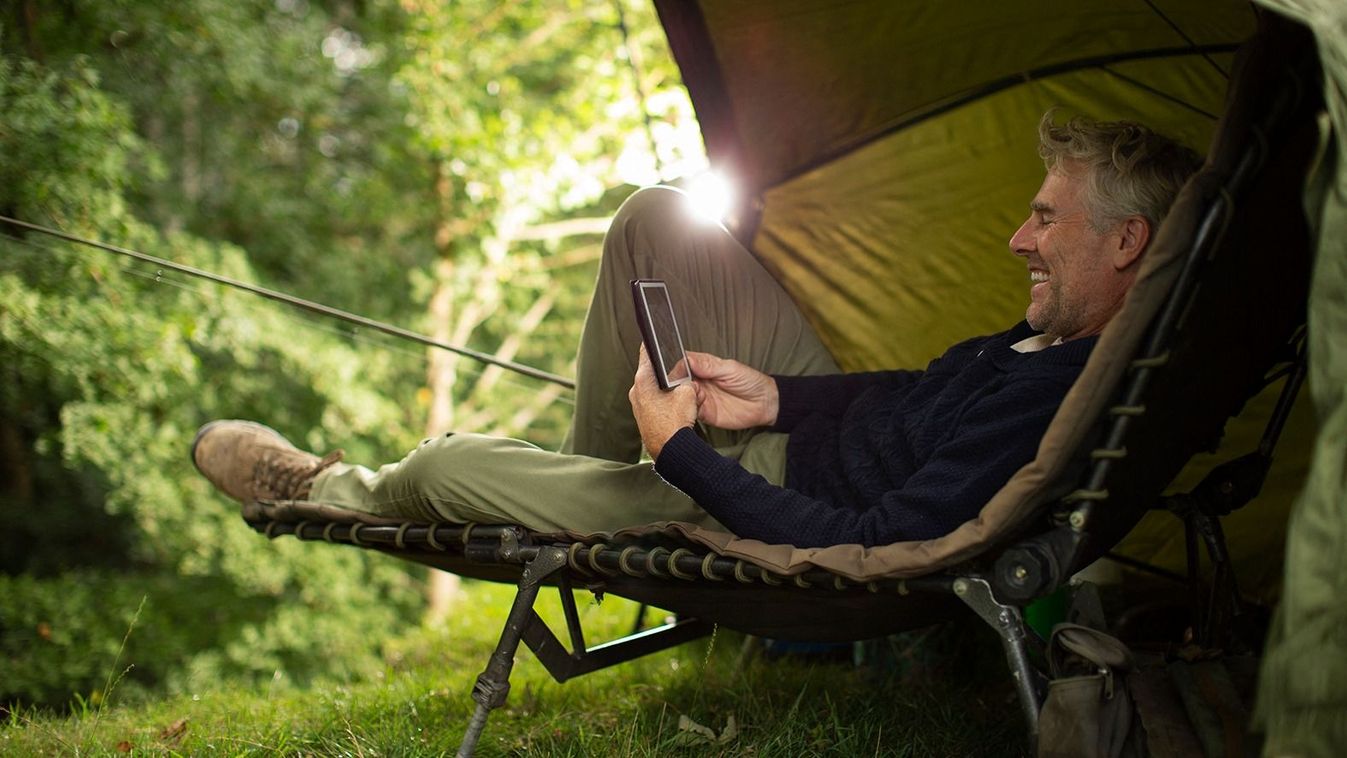 Man in camping lounge chair fishing and using digital tablet