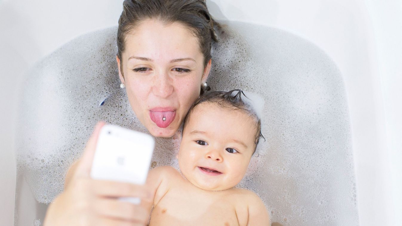 Mother using smartphone to photograph herself and baby while taking a bath