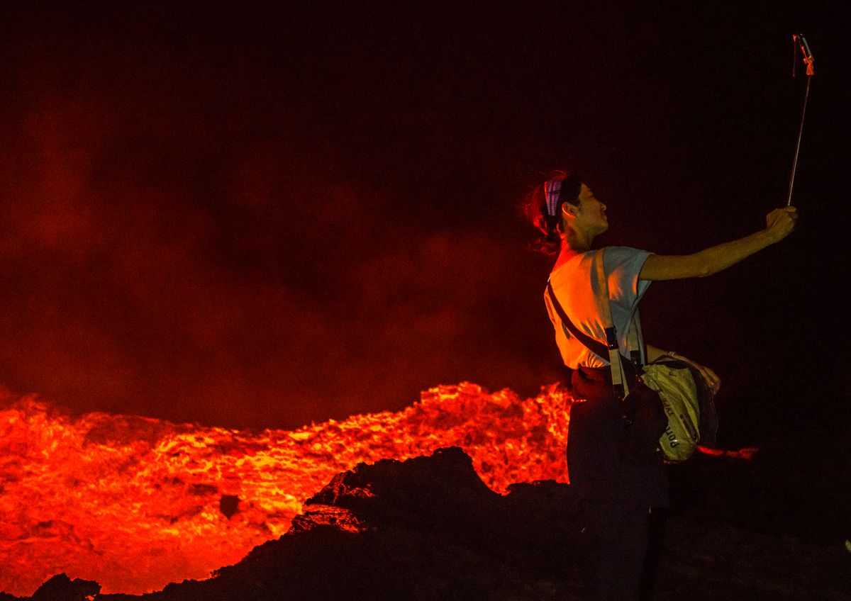 Tourist taking a selfie in front of the living lava lake in the crater of erta ale volcano, Afar region, Erta ale, Ethiopia