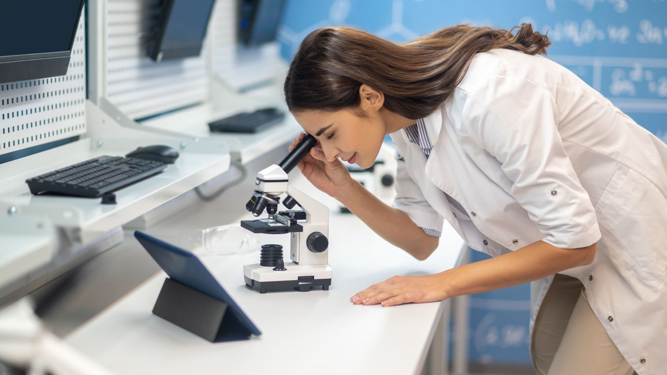 Woman leaning over microscope sideways to camera