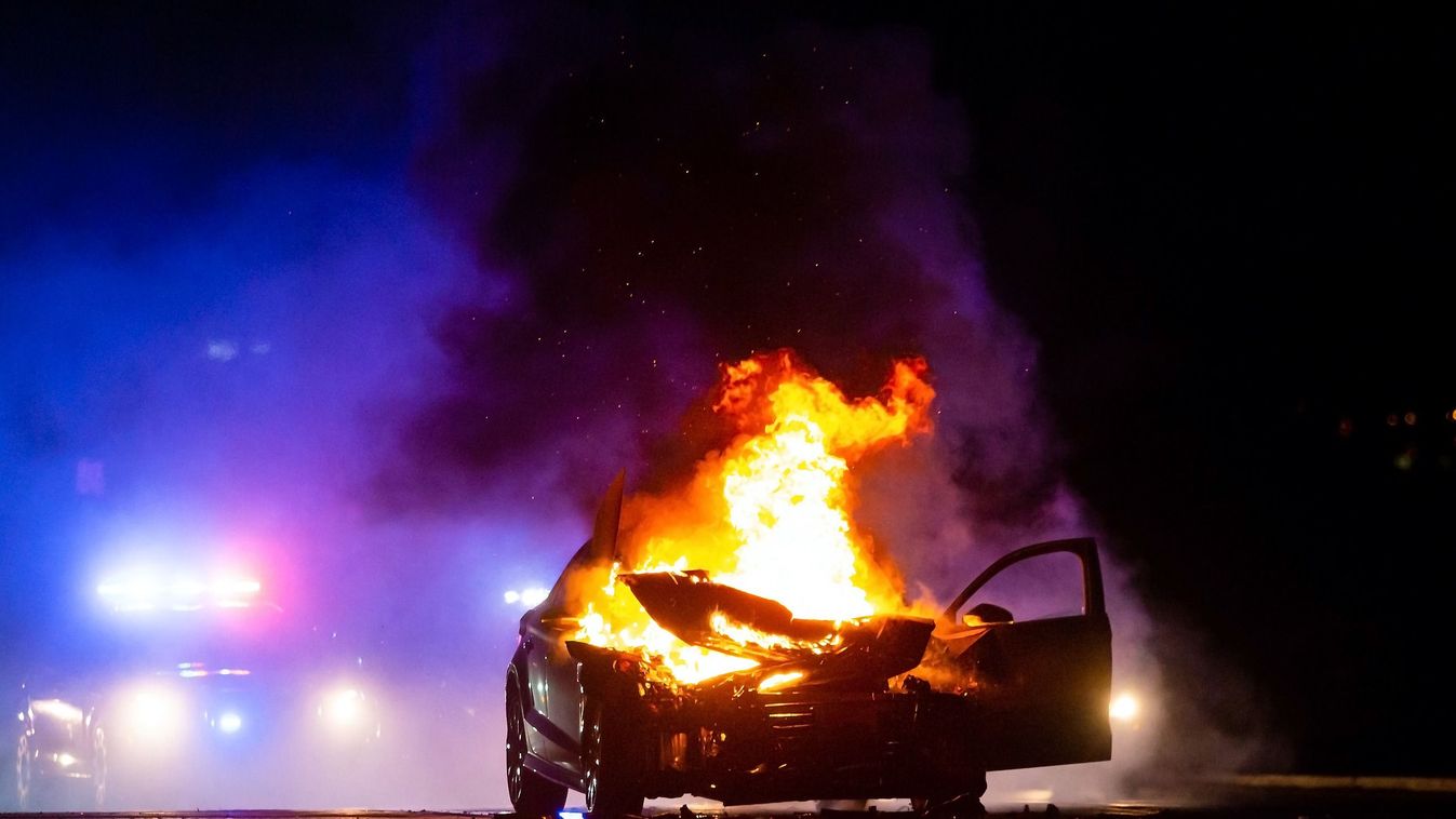Car,On,Fire,At,Night,With,Police,Lights,In,Background