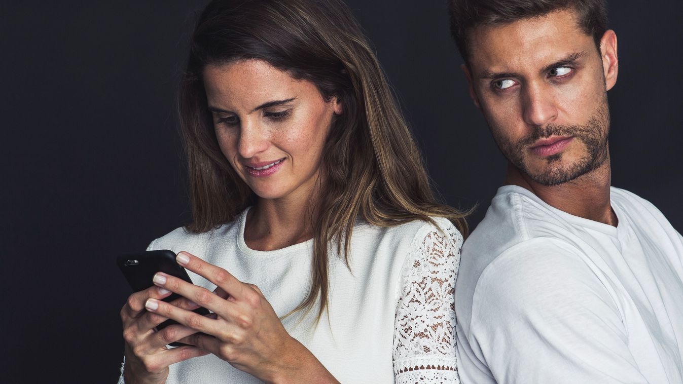 Man glaring over his shoulder as girlfriend uses smartphone