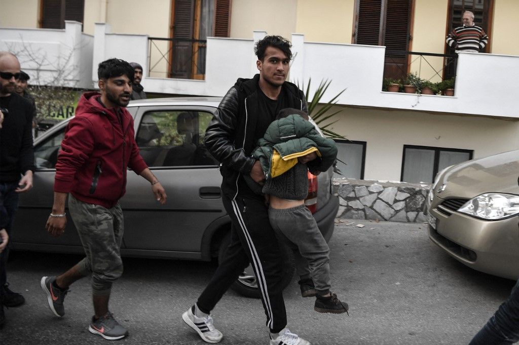 Egy migráns viszi gyermekét, miközben a rendőrök visszaszorítják a Moria táborból a migránsokat és menekülteket, akik a Leszbosz szigetén, Mytilene kikötője közelében gyűltek össze, abban a reményben, hogy 2020. március 4-én komppal indulnak Athénba. (Fotó: AFP/LOUISA GOULIAMAKI)
