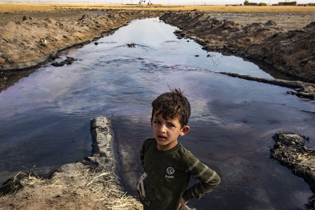 Egy gyerek egy közeli olajmező által szennyezett folyó partján, Rmeilan vidékén, Szíria északkeleti Hasakeh tartományában 2023. augusztus 14-én. (Fotó: AFP/Delil SOULEIMAN)