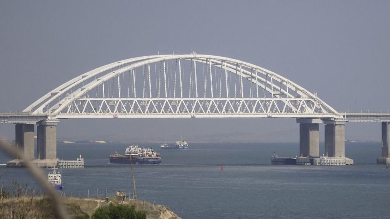 Teherhajók és autós kompok haladnak át a Kercsi-szoroson, mögötte a krími híd látható