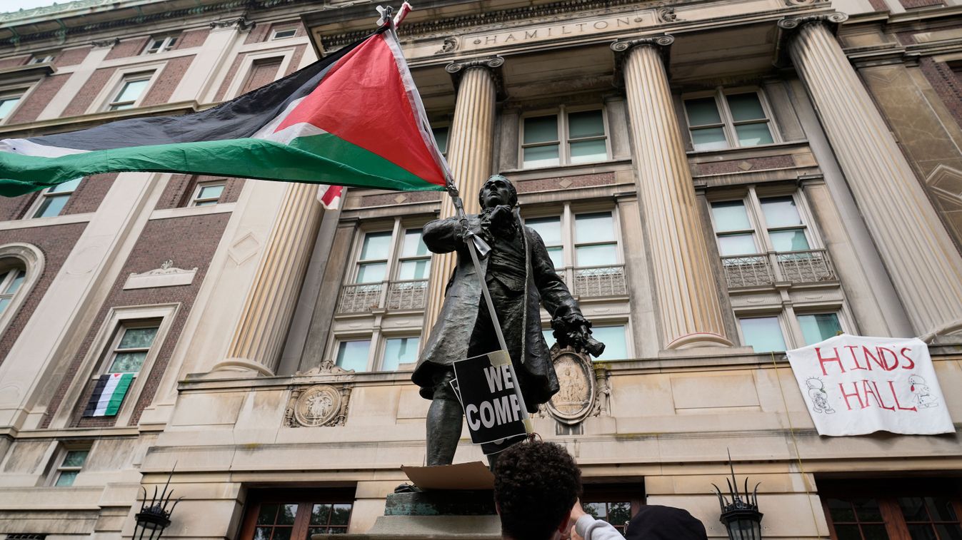 Palesztinpárti tüntető diák palesztin zászlót lenget a New York-i Columbia Egyetem Hamilton-csarnokának bejárata előtt 2024. április 30-án