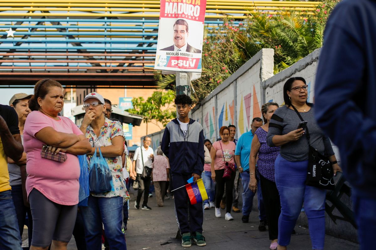 Sorban állnak szavazók a venezuelai elnökválasztáson, fölöttük Nicolás Maduro államfő és jelölt választási plakátja Caracasban 2024. július 28-án. (Fotó: MTI/AP/Cristian Hernández)