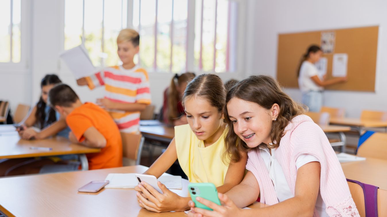 Girls,Sitting,At,Desk,In,Classroom,,Using,Smartphones,Together,During
Girls sitting at desk in classroom, using smartphones together during lesson in school.Illusztráció, gyerekek egy iskolában