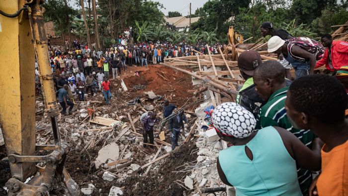 People look on as an excavator helps search for people trapped under debris after a landfill collapsed in Kampala on August 10, 2024. Eight people including two children were killed when mountains of garbage collapsed at a landfill in the Ugandan capital Kampala on August 10, the city authority said. (Photo by BADRU KATUMBA / AFP)