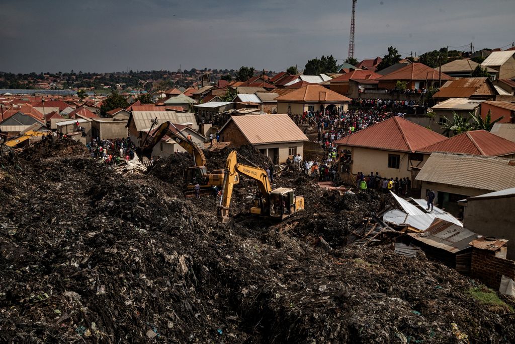 People look on as an excavator helps search for people trapped under debris after a landfill collapsed in Kampala on August 10, 2024. Eight people including two children were killed when mountains of garbage collapsed at a landfill in the Ugandan capital Kampala on August 10, the city authority said. (Photo by BADRU KATUMBA / AFP)