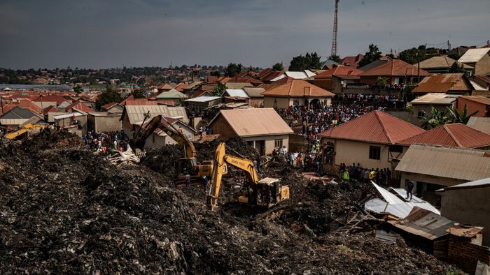 People look on as an excavator helps search for people trapped under debris after a landfill collapsed in Kampala on August 10, 2024. Eight people including two children were killed when mountains of garbage collapsed at a landfill in the Ugandan capital Kampala on August 10, the city authority said. (Photo by BADRU KATUMBA / AFP)