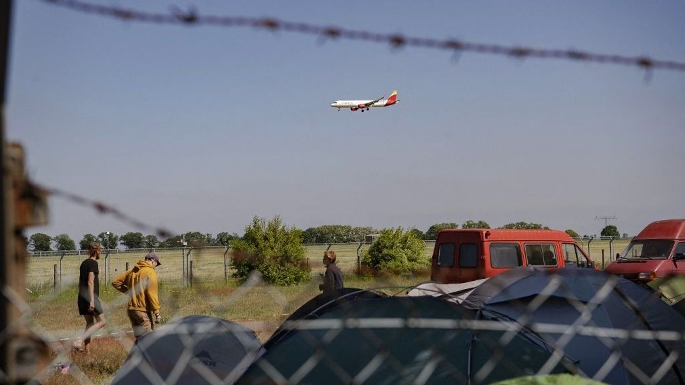 A „Prevent deportation center BER” kezdeményezés tiltakozó táborának résztvevői felállítják sátraikat, miközben egy repülőgép repül felettük.