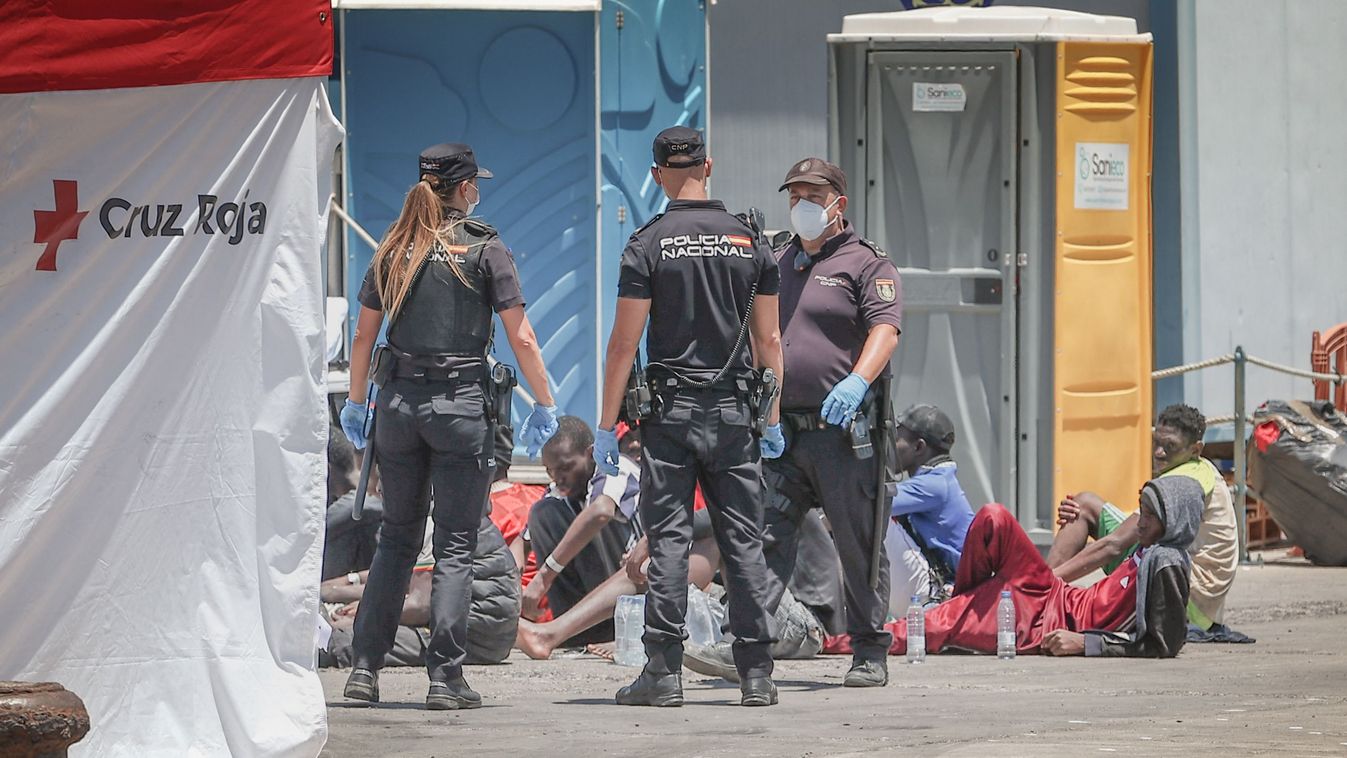 Police officers tend to migrants sitting near a Red Cross tent at Puerto de los Cristianos, on the Canary Island of Tenerife, on May 8, 2024. About 50 migrants, several of them in poor health, according to the Spanish Red Cross, have been intercepted by Maritime Rescue near La Tejita Beach, and taken to Puerto de los Cristianos on the Canary Island of Tenerife. (Photo by DESIREE MARTIN / AFP)