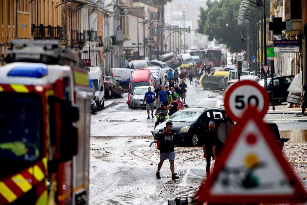 Residents walk next to piled up cars in a street covered in mud following floods in Valencia's De La Torre neighbourhood, eastern Spain, on October 30, 2024. Floods triggered by torrential rains in Spain's eastern Valencia region has left at least 62 people dead, rescue services said on October 30. (Photo by Ruben FENOLLOSA / AFP)