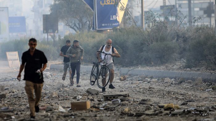 A man pushes his bicycle over the debris as others run along the old road leading to Beirut International airport on the outskirts of the capital, following an Israeli airstrike on October 6, 2024. A huge fireball lit up the night sky and plumes of smoke rose over south Beirut early on October 6 as Israel unleashed intense air strikes targeting Hezbollah, nearly a year since the Gaza war erupted. (Photo by AFP)