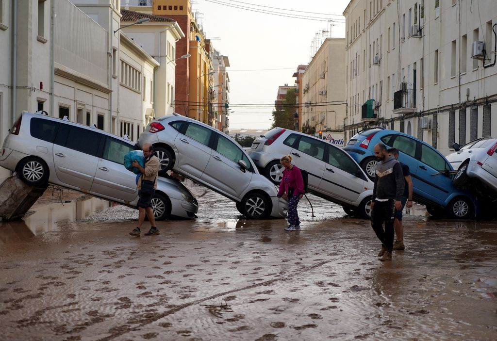 Residents walk past piled up cars following deadly floods in Valencia's De La Torre neighbourhood, south of Valencia, eastern Spain, on October 30, 2024. Floods triggered by torrential rains in Spain's eastern Valencia region has left at least 70 people dead, rescue services said on October 30. (Photo by Manaure QUINTERO / AFP)