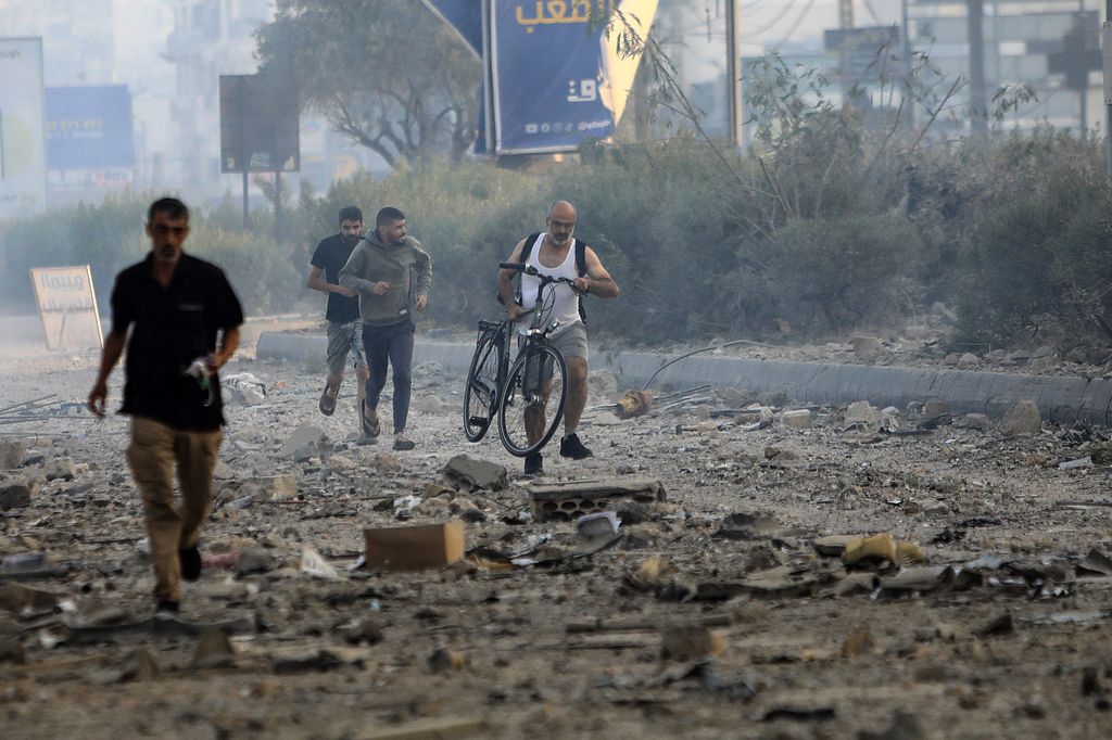 A man pushes his bicycle over the debris as others run along the old road leading to Beirut International airport on the outskirts of the capital, following an Israeli airstrike on October 6, 2024. A huge fireball lit up the night sky and plumes of smoke rose over south Beirut early on October 6 as Israel unleashed intense air strikes targeting Hezbollah, nearly a year since the Gaza war erupted. (Photo by AFP)