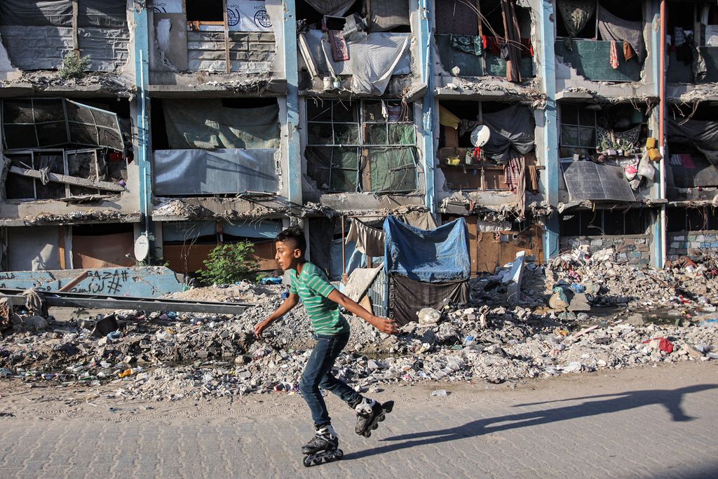 A boy roller-blades past a destroyed building at a camp sheltering people displaced by conflict in Jabalia in the northern Gaza Strip on September 8, 2024 amid the ongoing war in the Palestinian territory between Israel and Hamas. (Photo by Omar AL-QATTAA / AFP)