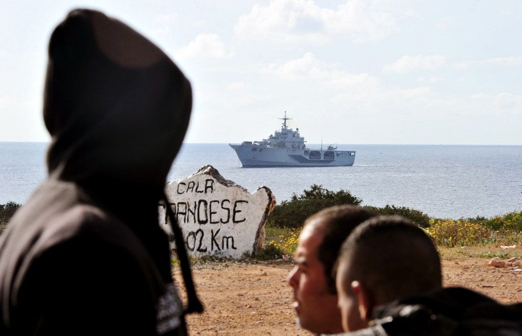 Tunéziai migránsok a San Marco olasz haditengerészeti hajó mellett az olaszországi Lampedusa sziget kikötőjében