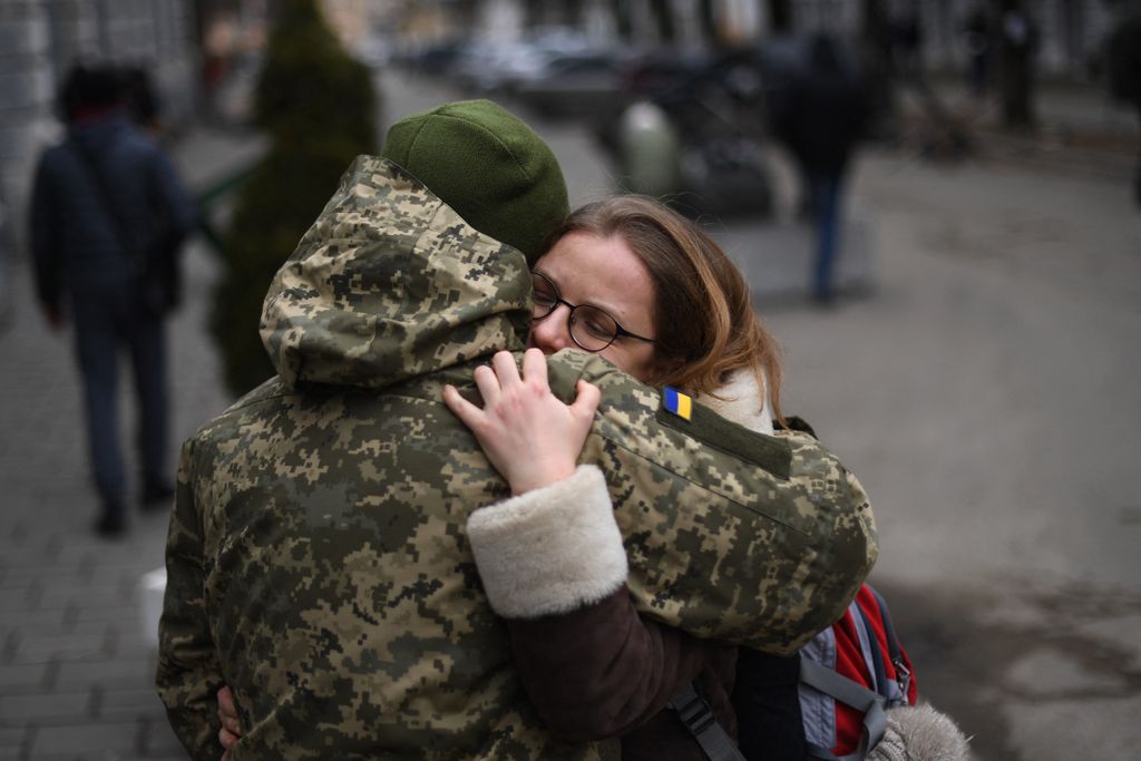 An Ukrainian soldier hugs his partner next to a military base where residents are queuing to join the army, in Lviv on March 2, 2022. Russia steps up its bombing campaign and missile strikes on Ukraine's cities on March 2, 2022. (Photo by Daniel LEAL / AFP)