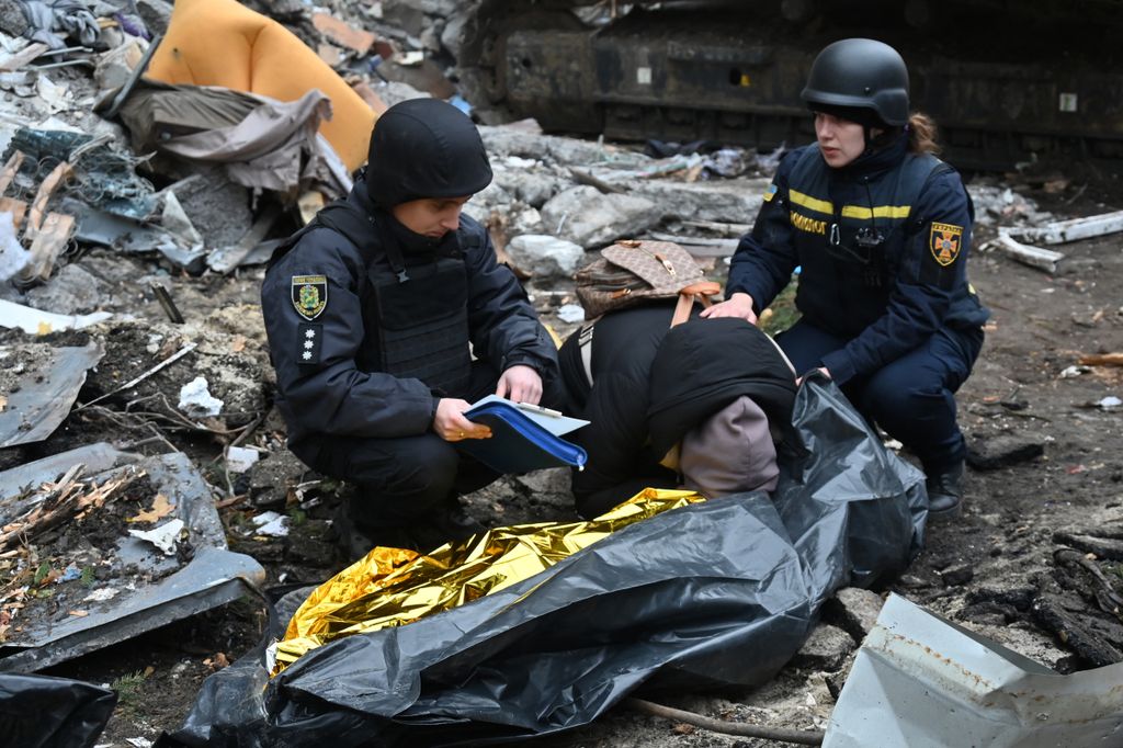 Ukrainian law enforcement officers comfort a woman crying over the body of her 15-year-old son following a missile attack in Kharkiv on October 31, 2024. Two children were among three killed in a Russian bombardment of an apartment building in Ukraine's second city of Kharkiv, with dozens more injured, the local governor said on October 31, 2024. (Photo by SERGEY BOBOK / AFP)