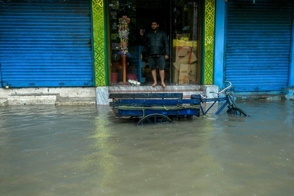 A man stands at his shop along a flooded street as it rains ahead of a cyclonic storm in Chennai on November 30, 2024. (Photo by R.Satish BABU / AFP)