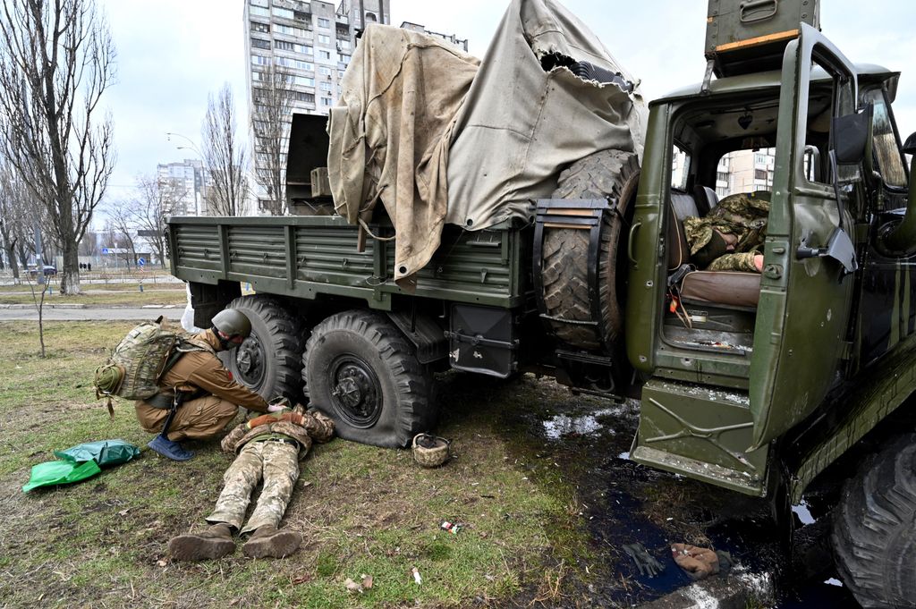 EDITORS NOTE: Graphic content / An Ukrainian military medic (L) examines the body of a Russian serviceman wearing a Ukranian service uniform lying beside a vehicle after he and members from a raiding party were shot during a skirmish in the Ukrainian capital of Kyiv on February 25, 2022, according to Ukrainian service personnel at the scene. Russian forces are approaching Kyiv from the north and northeast, Ukraine's army said, with rising fears the capital could fall on the second day of Moscow's offensive. (Photo by Sergei SUPINSKY / AFP)