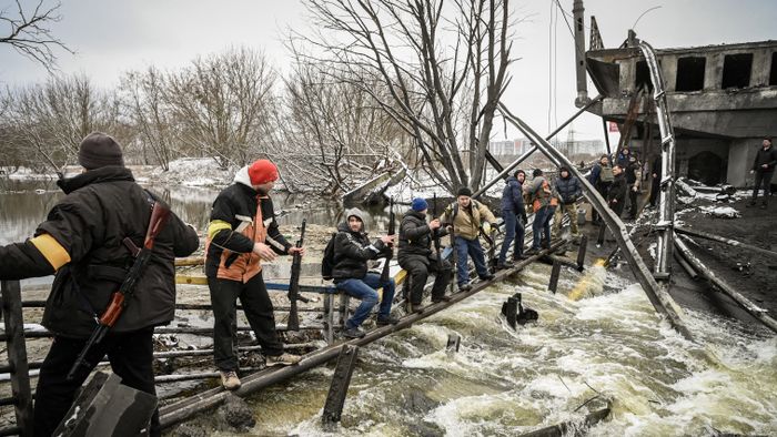 Members of a Ukrainian civil defense unit pass new assault rifles to the opposite side of a blown up bridge on Kyiv’s northern front on March 1, 2022. Satellite photos showed on March 1, 2022, a Russian convoy stretching for dozens of kilometers and advancing slowly toward the Ukrainian capital : according to the Ukrainian general staff, Moscow is gathering its forces for an assault on Kiev and other major cities while international retaliatory measures against Russia continued to accumulate. (Photo by ARIS MESSINIS / AFP)