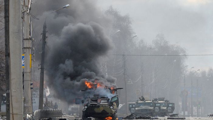 An unidentified soldier's body lies near a burning Russian Armoured personnel carrier (APC) during fighting with the Ukrainian armed forces in Kharkiv, on February 27, 2022. Ukrainian forces secured full control of Kharkiv on February 27, 2022 following street fighting with Russian troops in the country's second biggest city, the local governor said. (Photo by Sergey BOBOK / AFP)