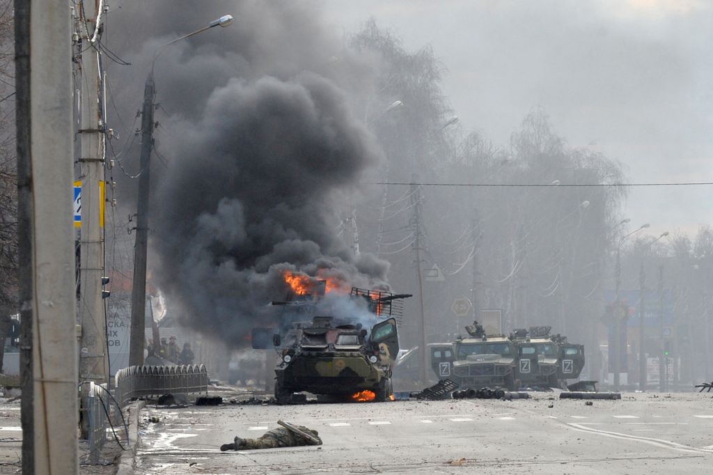 An unidentified soldier's body lies near a burning Russian Armoured personnel carrier (APC) during fighting with the Ukrainian armed forces in Kharkiv, on February 27, 2022. Ukrainian forces secured full control of Kharkiv on February 27, 2022 following street fighting with Russian troops in the country's second biggest city, the local governor said. (Photo by Sergey BOBOK / AFP)