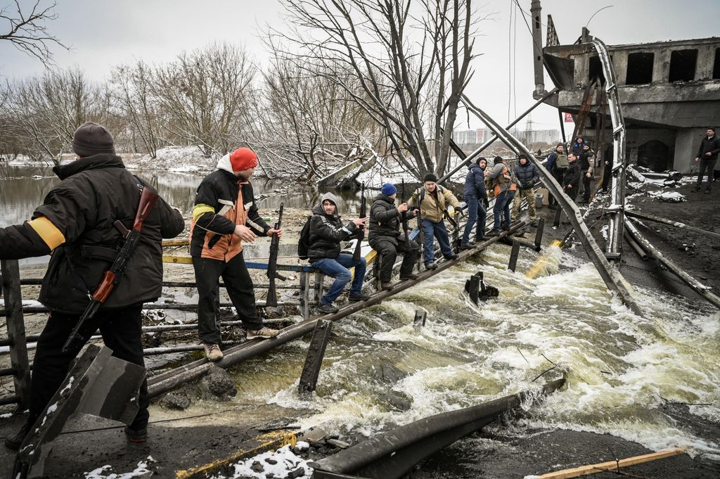 Members of a Ukrainian civil defense unit pass new assault rifles to the opposite side of a blown up bridge on Kyiv’s northern front on March 1, 2022. Satellite photos showed on March 1, 2022, a Russian convoy stretching for dozens of kilometers and advancing slowly toward the Ukrainian capital : according to the Ukrainian general staff, Moscow is gathering its forces for an assault on Kiev and other major cities while international retaliatory measures against Russia continued to accumulate. (Photo by ARIS MESSINIS / AFP)