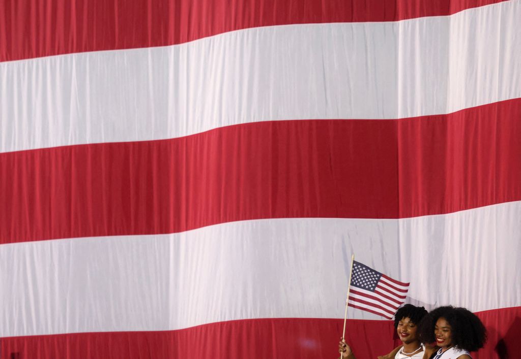 Supporters of US Vice President and Democratic presidential candidate Kamala Harris standing beneath a giant US flag wave small flags during an election night event at Howard University in Washington, DC, on November 5, 2024. (Photo by CHARLY TRIBALLEAU / AFP)