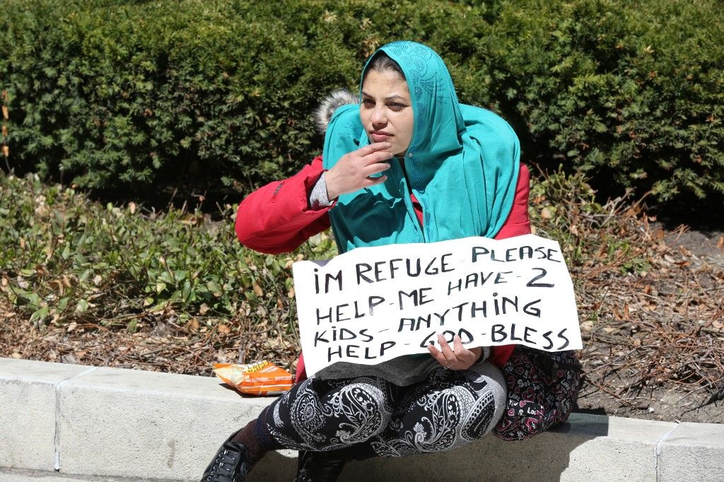 Egy szír menekült egy táblát tart a kezében, melyen pénzt kér a járókelőktől Toronto belvárosában, Ontario államban, Kanadában