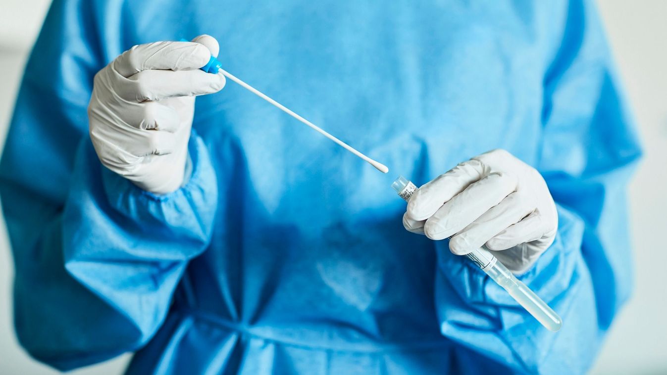 Midsection of female doctor with swab test sample during COVID-19 crisis. Female medical professional is holding test tube in hospital. She is wearing protective suit.