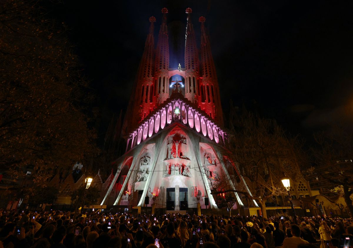 People watch a light show projected on the facade of Spanish architect Antoni Gaudi's Sagrada Familia Basilica, marking the start of the Holy Week, in Barcelona on April 14, 2025. The Catholic Church has put Antoni Gaudi, the designer of Barcelona's Sagrada Familia basilica nicknamed "God's architect", on the path to sainthood, the Vatican said today. Pope Francis recognised the Catalan architect's "heroic virtues" and authorised a decree declaring him "venerable", the Vatican said in a statement. (Photo by LLUIS GENE / AFP)