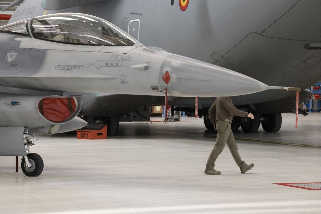 A Belgian military member walks past a F-16 fighter jet and an Airbus A400M Atlas aircraft during Ukrainian President Volodymyr Zelensky official visit after Belgium committed to deliver 30 of them to help Kyiv battle Russia's invasion, at Melsbroek military airport on May 28, 2024. Zelensky visits Belgium to ink the latest in a string of security accords with Western allies. Belgium committed to delivering 30 F-16 fighter jets by 2028 to help Kyiv battle Russia's invasion. (Photo by SIMON WOHLFAHRT / AFP)