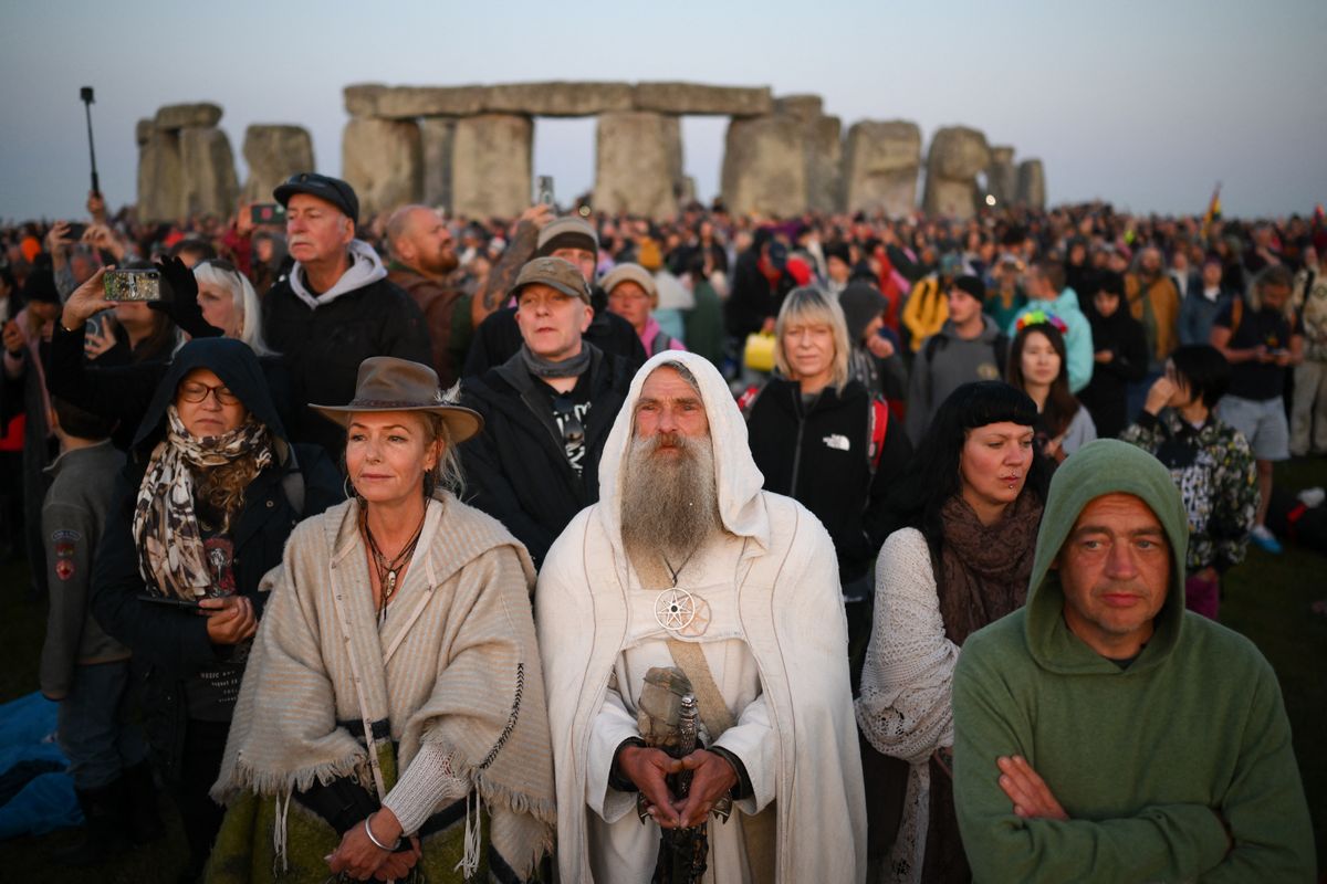 Revellers stand by the stones as they watch the sunrise at Stonehenge, near Amesbury, in Wiltshire, southern England on June 21, 2023, to celebrate the celebrate the Summer Solstice festival, which dates back thousands of years, celebrating the longest day of the year when the sun is at its maximum elevation. The stone monument -- carved and constructed at a time when there were no metal tools -- symbolises Britain's semi-mythical pre-historic period, and has spawned countless legends. (Photo by Daniel LEAL / AFP)