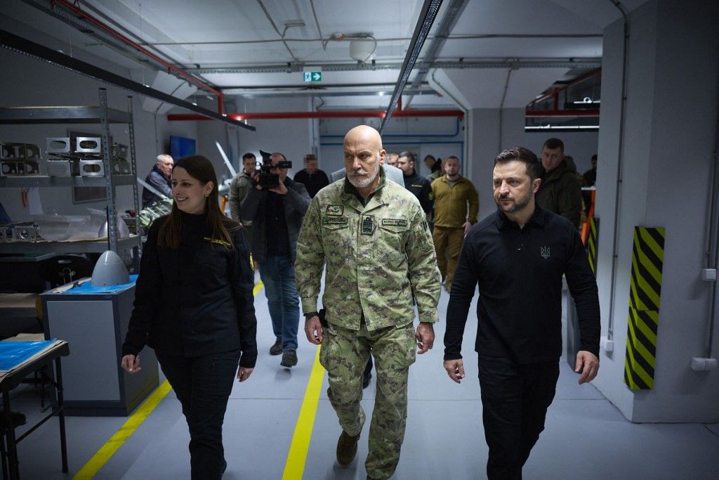 This handout photograph taken and released by Ukrainian Presidential Press Service on February 8, 2025, shows Ukrainian President Volodymyr Zelensky (R) and the Chair of the NATO Military Committee Giuseppe Cavo Dragone (C) during their during a visit to a defense industry enterprise, in an undisclosed location in Ukraine. President Volodymyr Zelensky met with the Chair of the NATO Military Committee, Giuseppe Cavo Dragone, who made his first foreign visit in this position specifically to Ukraine. At one of the defense industry enterprises, they got acquainted with the production capacities and characteristics of Ukrainian long-range weapons and spoke with the people working there. (Photo by Handout / UKRAINIAN PRESIDENTIAL PRESS SERVICE / AFP) / RESTRICTED TO EDITORIAL USE - MANDATORY CREDIT "AFP PHOTO / Ukrainian Presidential Press Service" - NO MARKETING NO ADVERTISING CAMPAIGNS - DISTRIBUTED AS A SERVICE TO CLIENTS