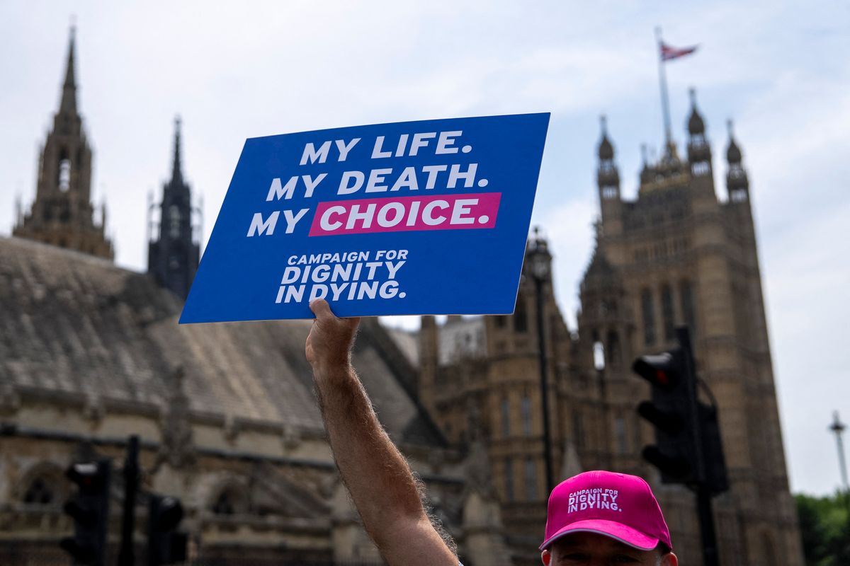 A campaigner for a change in the law on assisted dying holds a placard outside The Palace of Westminster, home to the Houses of Parliament in central London, on June 20, 2025, as MPs hold a knife-edge vote on whether to allow assisted dying for terminally ill people. (Photo by CARLOS JASSO / AFP)