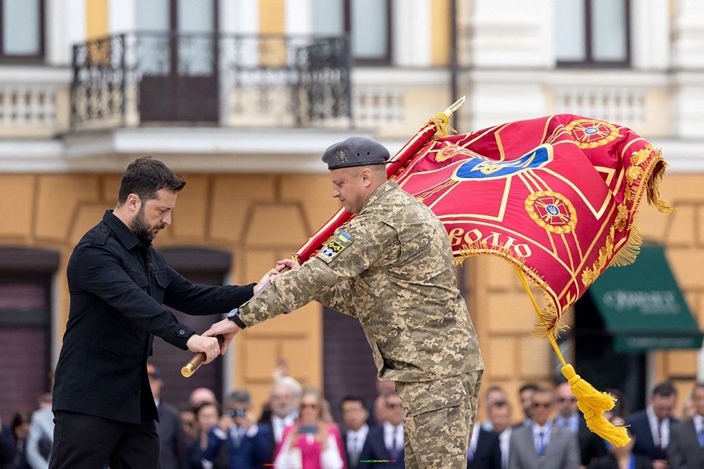 Volodimir Zelenszkij ukrán elnök (B) harci zászlót nyújt át egy egység parancsnokának az ukrán alkotmány napja alkalmából Kijevben (Fotó: AFP)